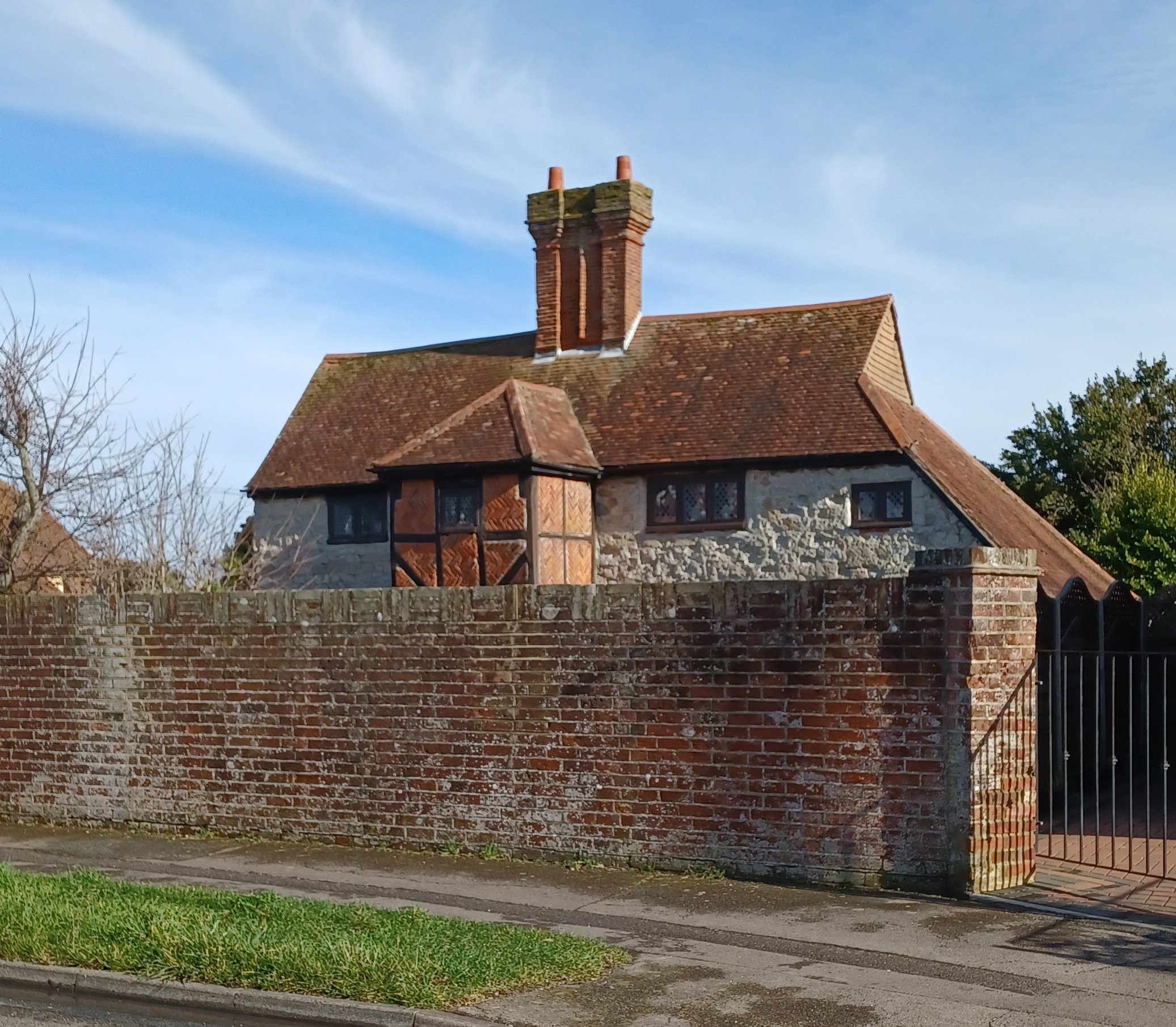 An old building with Elizabethan chimneys and a gable roof stands behind a brick wall