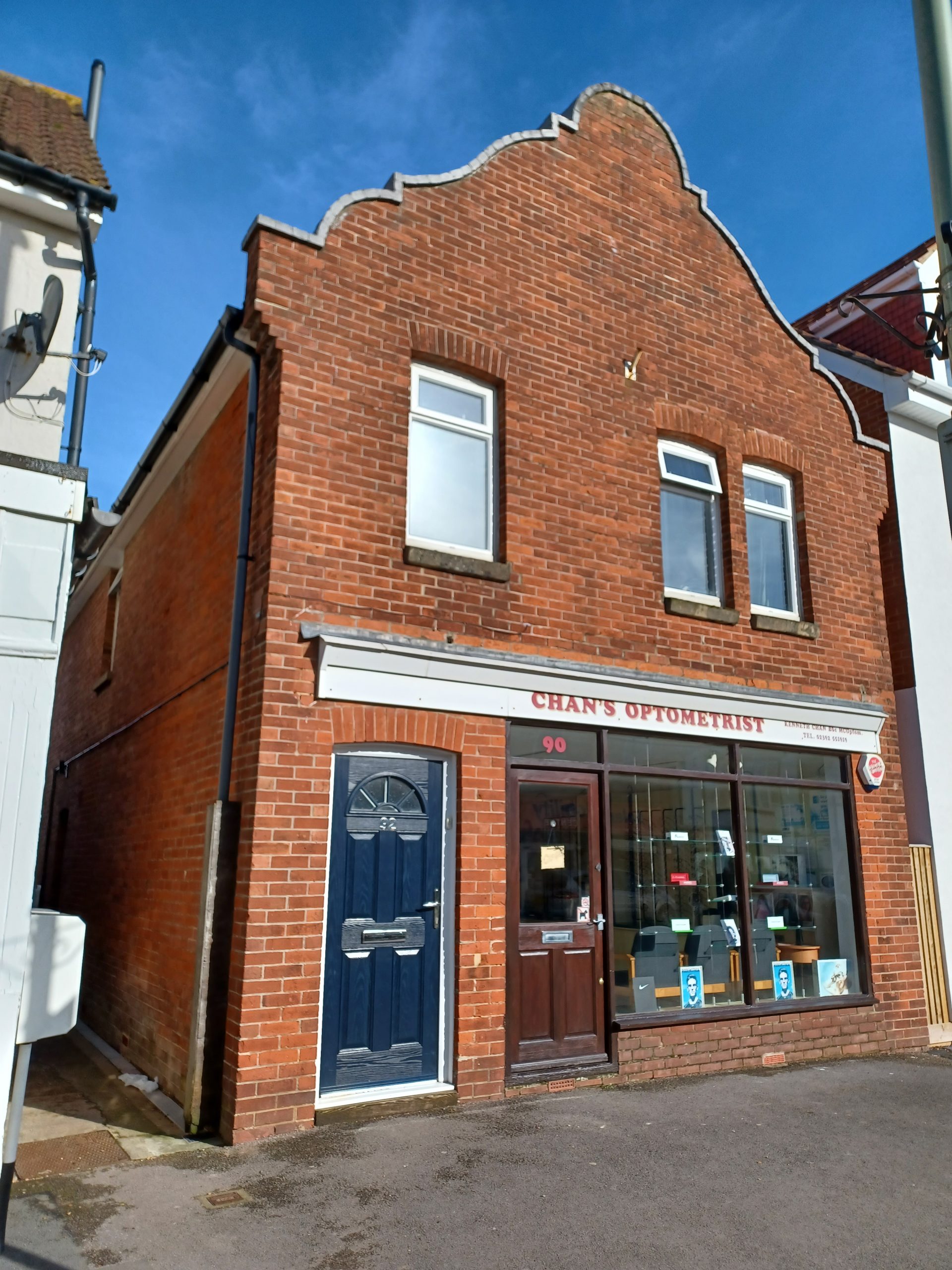 Shop front with ornate brickwork. The sin reads CHAN'S OPTOMERIST. At the left of the shop entrance is a black door that leas to private accommodation