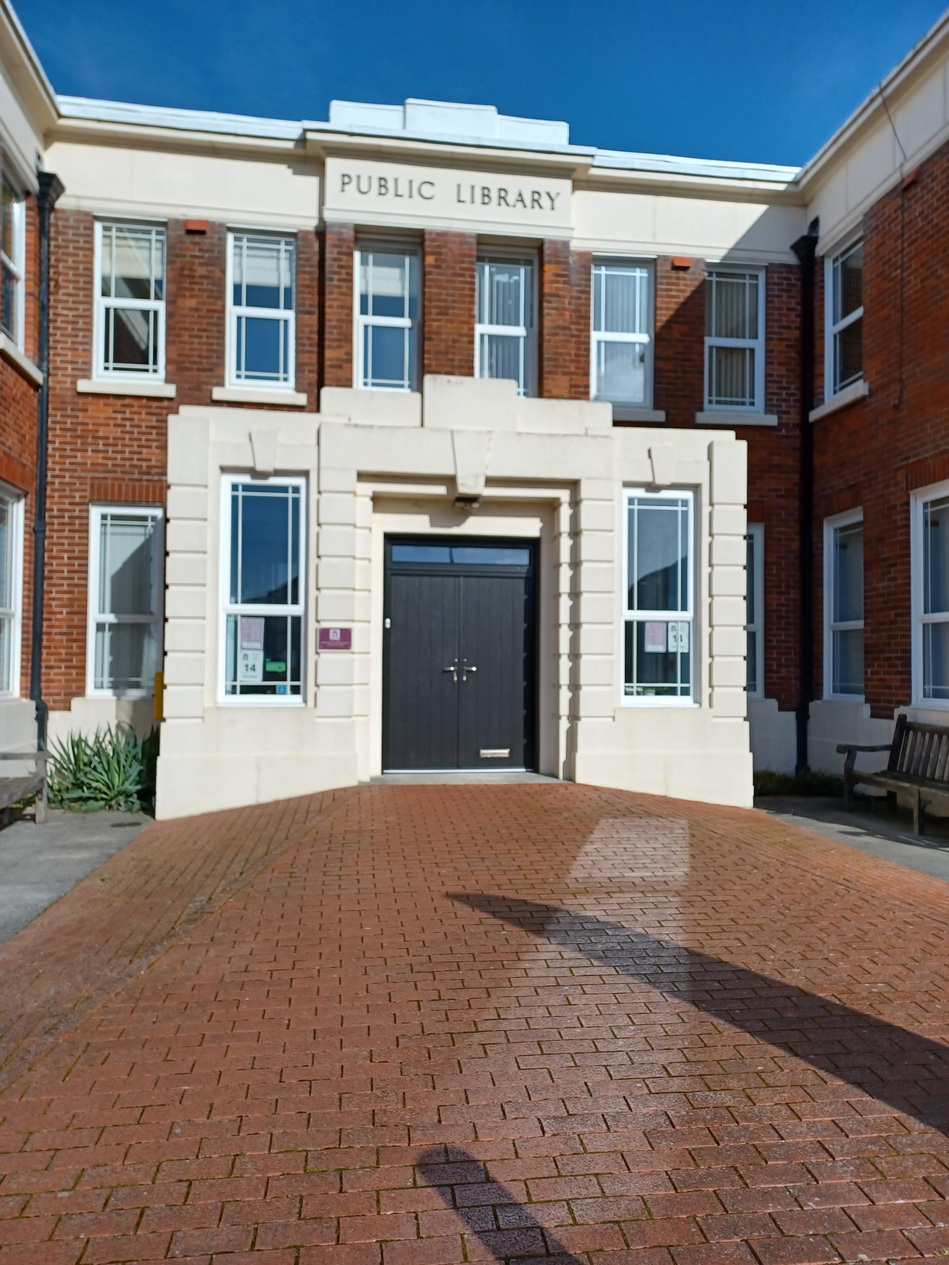 An Art Deco building.in the foreground is brick paving. At the top of the building are the words PUBLIC LIBRARY.