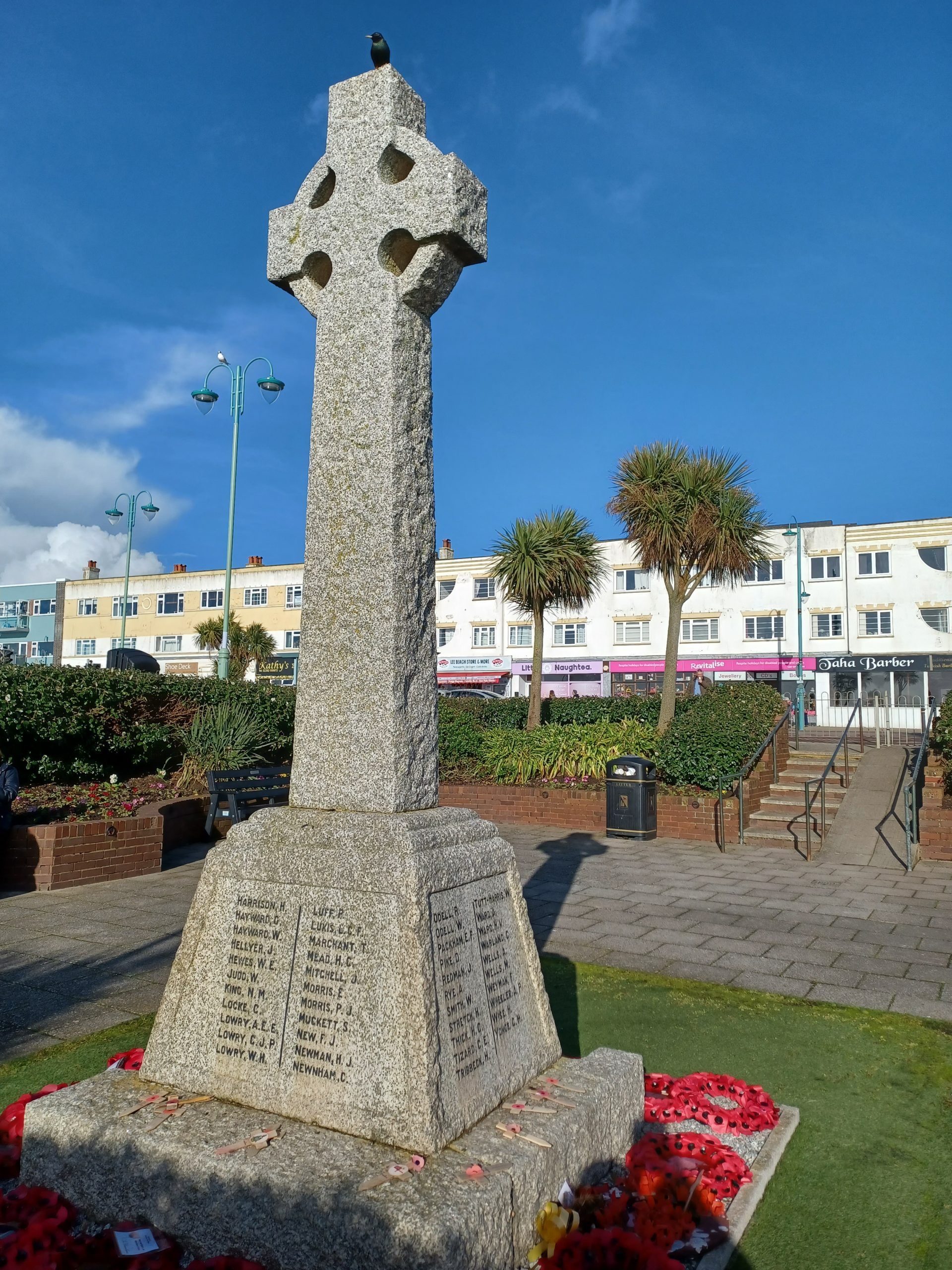 A Celtic memorial cross in a sunken garden. A row of shops and cafes can be seen in the background